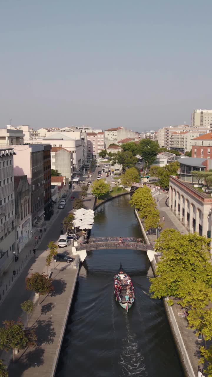 Barca Moliceiro che naviga sotto un ponte pedonale ad Aveiro, Portogallo. Aerea verticale