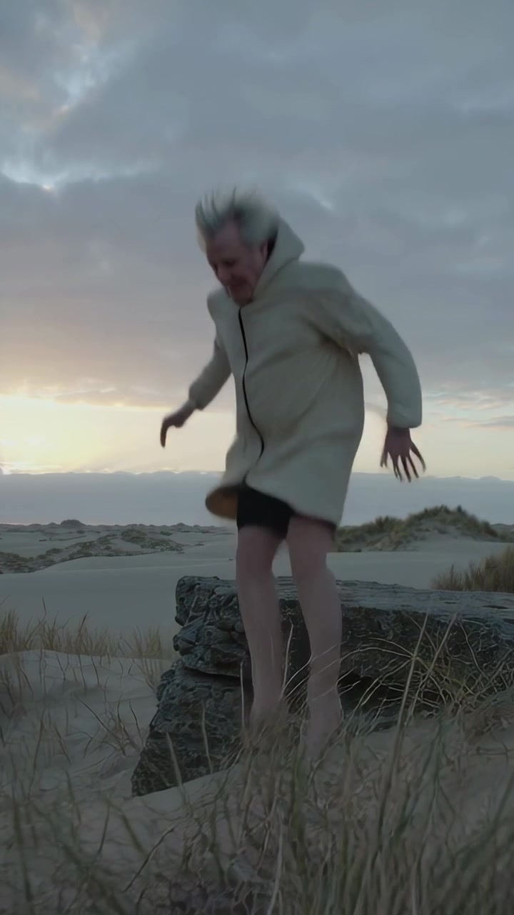Vertical video: Jumping elder man landing on low rock readying descent walking dunes