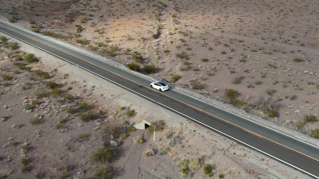 antena cinematográfica de un vehículo eléctrico blanco que conduce en piloto automático en una carretera vacía del desierto en nevada