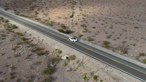 cinematic-overhead-aerial-of-white-electric-vehicle-driving-on-autopilot-on-an-empty-desert-road-in-Nevada