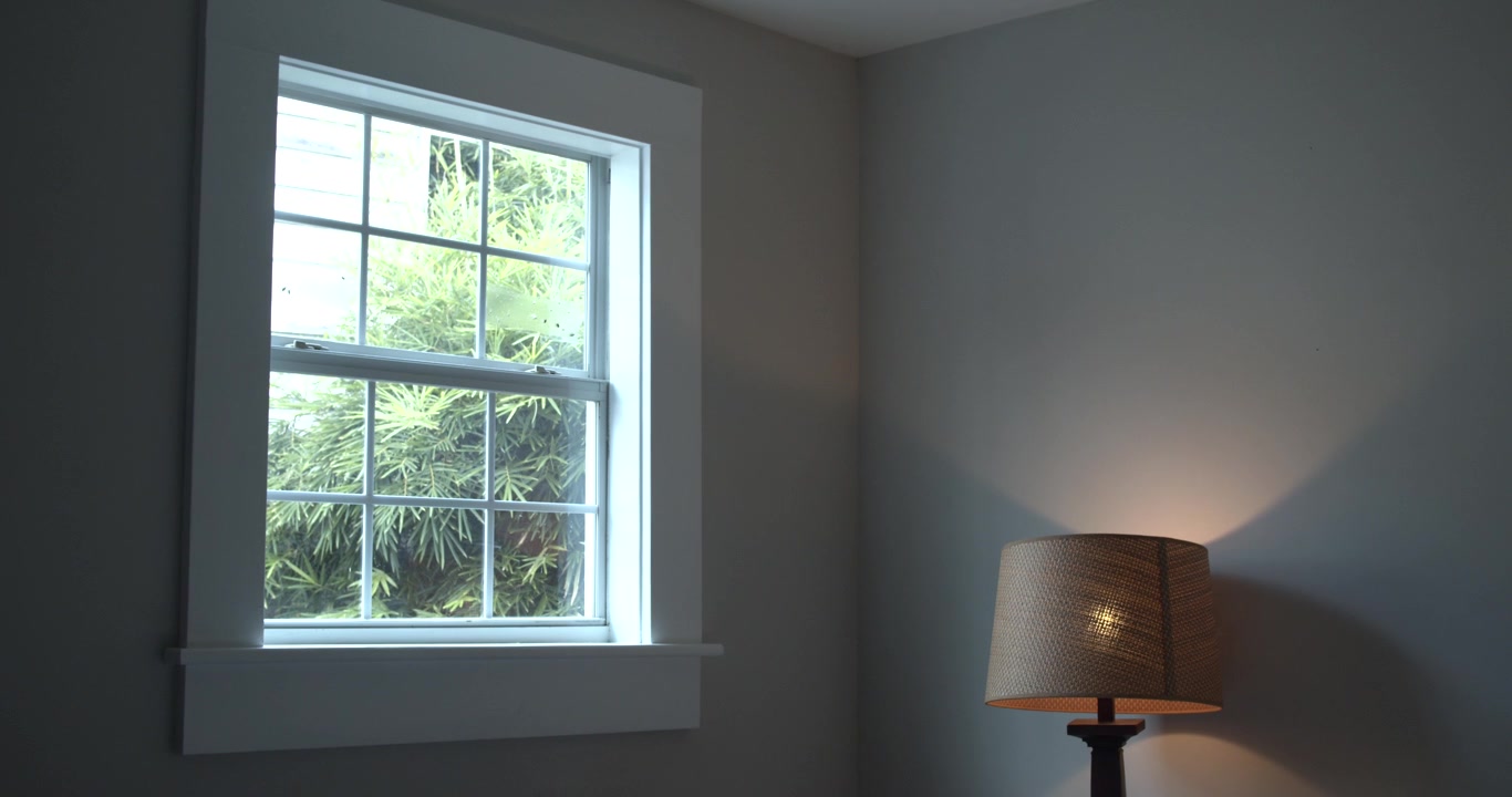 Natural light enters a quiet room through a window overlooking green trees. Minimal interior scene creating a calm atmosphere for home, lifestyle, and residential concepts.
