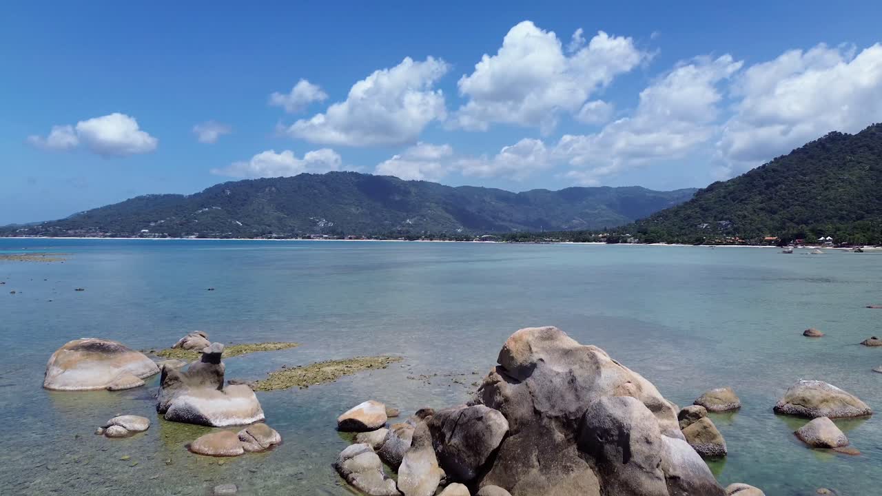 Aerial drone footage of Lamai Beach in Koh Samui, Thailand, featuring turquoise ocean, rocky shoreline, tropical island horizon, and scenic coastal landscape under clear tropical skies