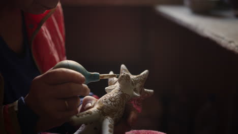 elderly woman putting dots on product in pottery. lady decorating toy moose