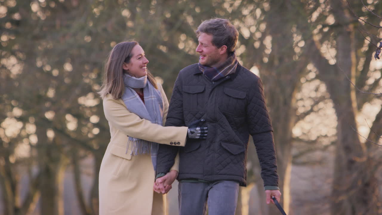 Paar mit Frau mit Handprothese zu Fuß Hund durch Winter- oder Herbstlandschaft
