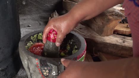 a mexican woman crushing tomatoes on a molcajete