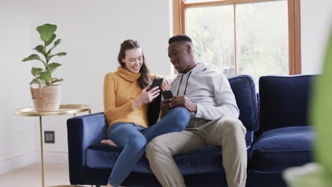 happy diverse couple sitting on sofa, using smartphone and credit card in home,copy space