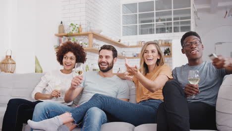 group of friends sitting on sofa and watching movie at home whilst drinking wine