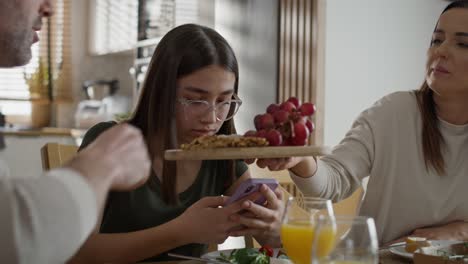 addicted teenage girl using mobile phone during breakfast at the table