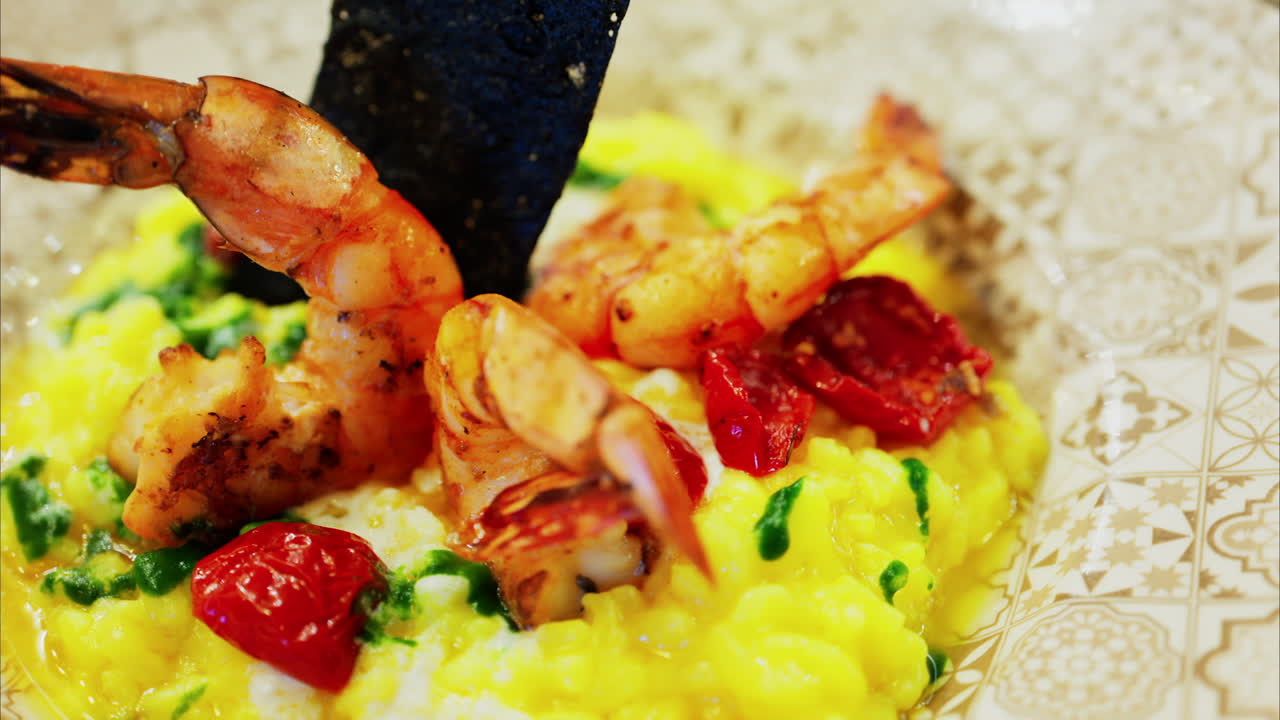 Close up of saffron risotto topped with grilled prawns and roasted cherry tomatoes