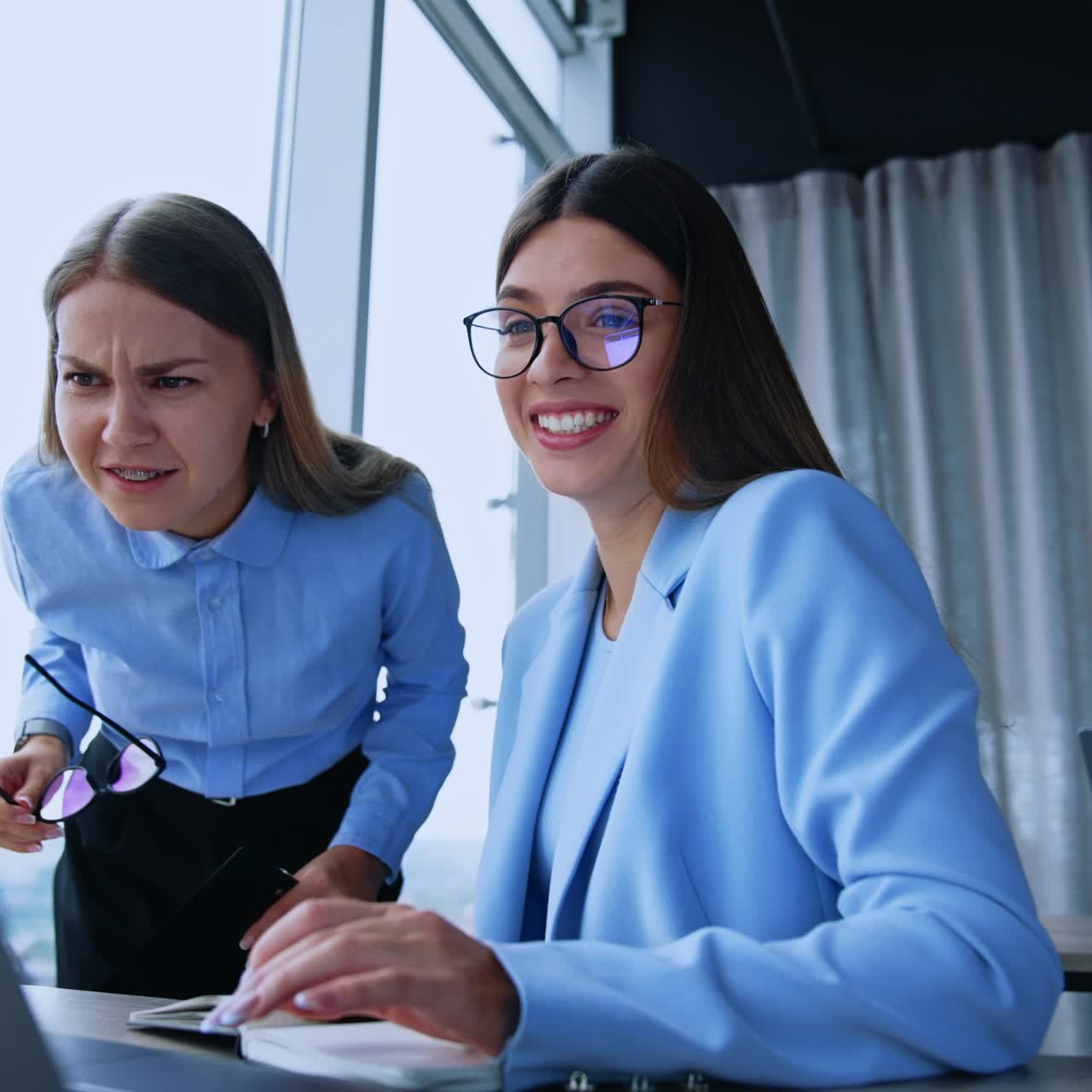 Happy resilient female employees in the modern office. Ladies look at the laptop screen smiling and getting surprised. Low angle view