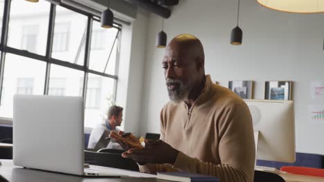 African-american-businessman-sitting-at-table-and-using-laptop-at-office