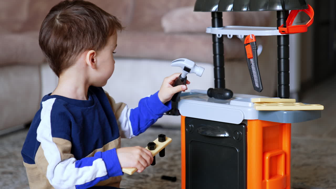 Child plays with toy tools at home. A young boy sits on the floor, engaging with toy tools near a play kitchen setup, displaying focus and creativity