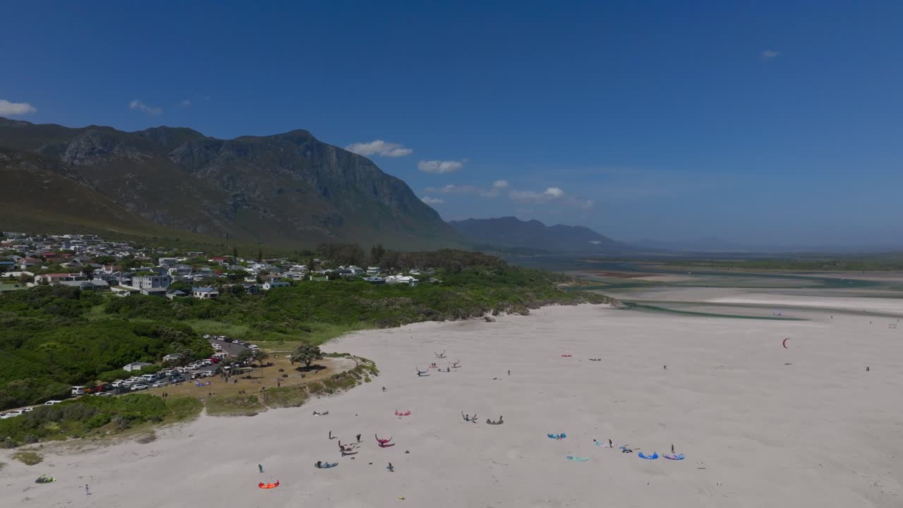 Wide beach view in Hermanus with kitesurfers, swimmers, golden sand, and scenic mountains