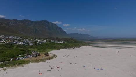wide beach view in hermanus with kitesurfers, swimmers, golden sand, and scenic mountains