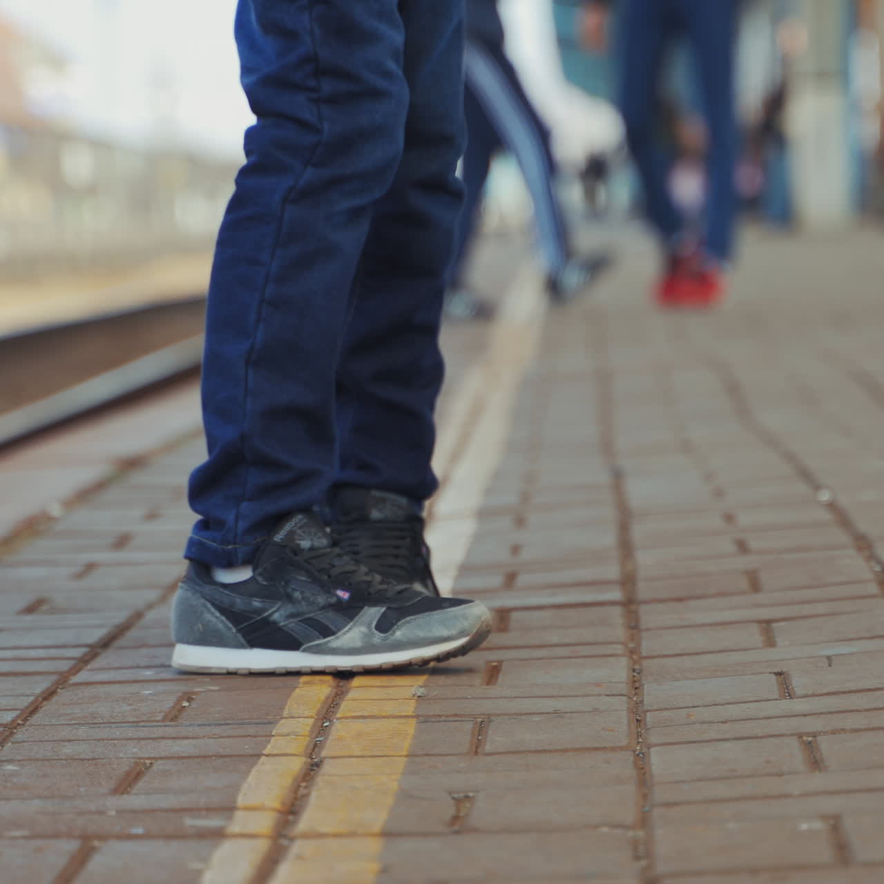 Young boy in jeans and trainers is waiting for express train on railway station platform. Boy's legs going forward and backward on the pavement. Close-up