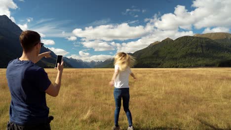 Influencer-Paar-Macht-Foto-Mit-Mobiltelefon,-Während-Schönes-Mädchen-Auf-Offenen-Grasebenen-Mit-Blick-Auf-Ausgedehnte-Bergtäler-Rotiert