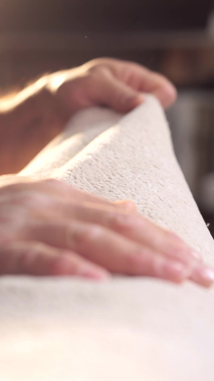 Die Sequenz beginnt mit dem beleuchteten und weichen Rand eines hellen Stoffes; dann sind Hände zu sehen, die sanft über die Oberfläche gleiten und deren gleichmäßige Textur und perfekte Verarbeitung prüfen.