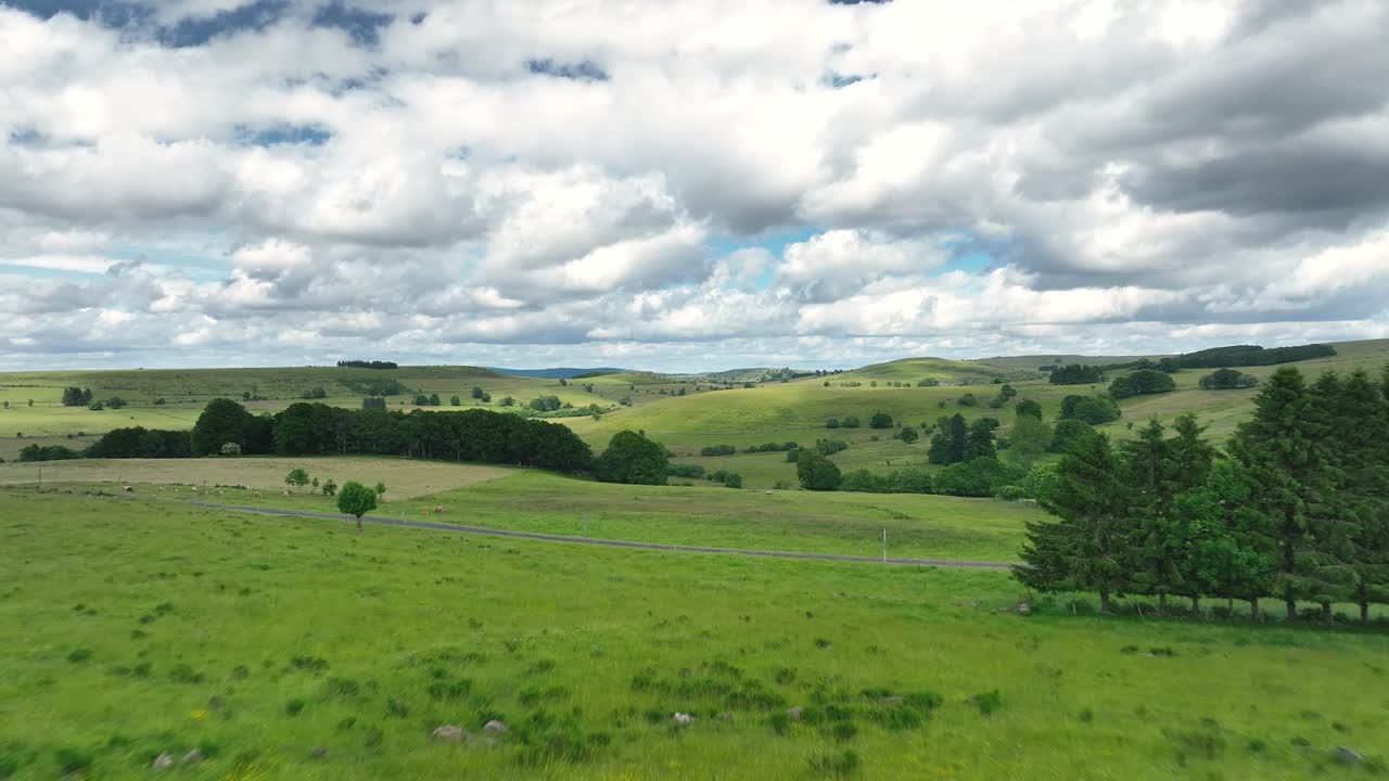 Espectacular vídeo aéreo grabado con dron de frondosos pastos verdes y colinas onduladas en la meseta de Aubrac en Francia, que capta el tranquilo paisaje rural bajo un cielo nublado.