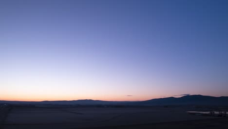 Sunrise-time-lapse,-soft-orange-glow-brightens-a-dark-blue-desert-morning-sky,-aerial-hyperlapse