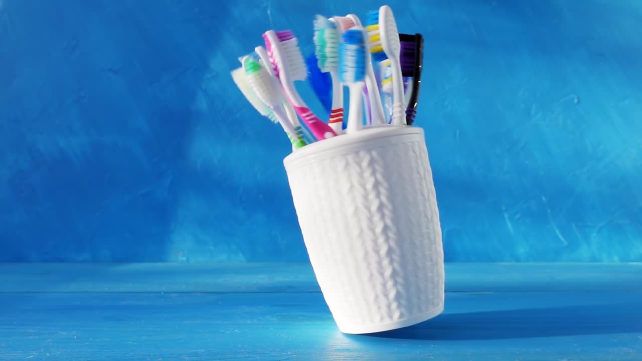 Many different toothbrushes in a white cup swirl on a table against a blue background. 4k creative raw loop video with speed ramp effect. Filmed on high speed cinema camera, 1000fps.