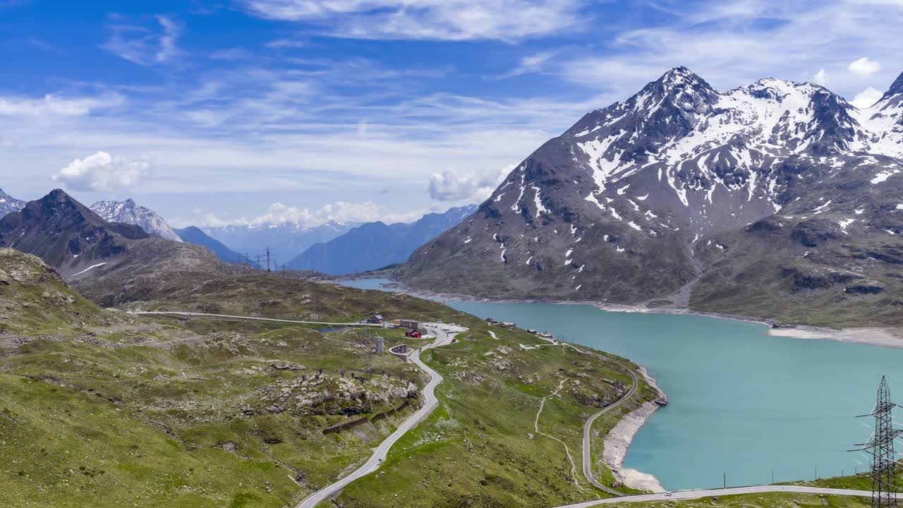 Kıvrımlı bir yol, turkuaz bir göl ve karla kaplı dağları gösteren Bernina Geçidi manzarası. Havadan çekim, hyperlapse.