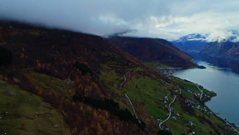 Carretilla-Aérea-Que-Revela-Un-Paisaje-Otoñal-De-Los-Fiordos-Y-Un-Pequeño-Pueblo-En-La-Ladera-De-La-Montaña-En-Noruega