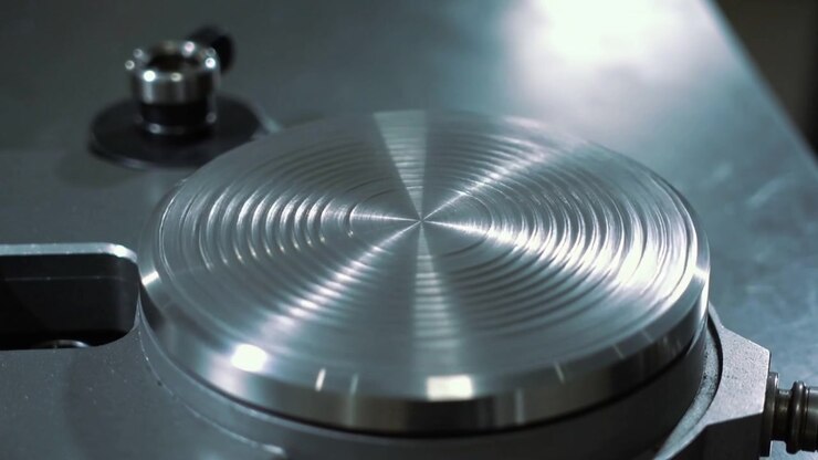Spinning rotary fixture moving metal disc showing lathe marks catching light in shop, clamping knob