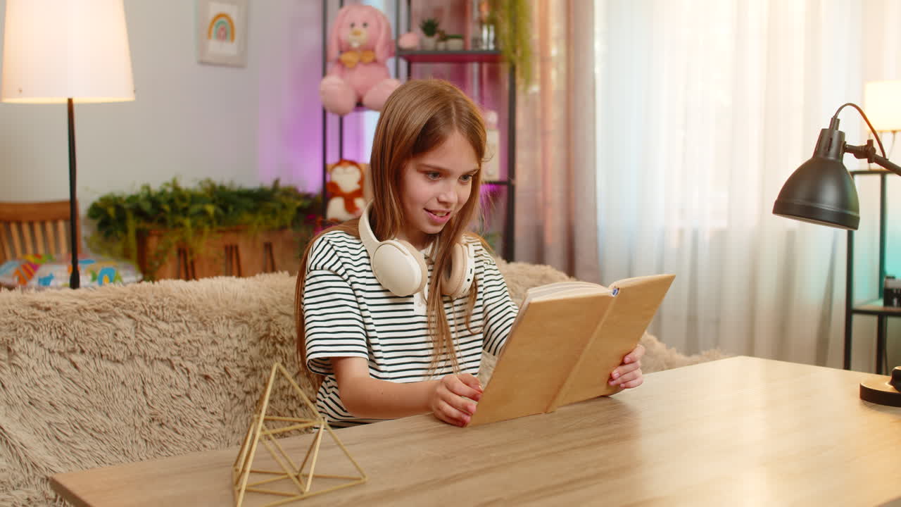 Child girl kid joyfully pretends to be roaring dinosaur while reading book at table on home sofa