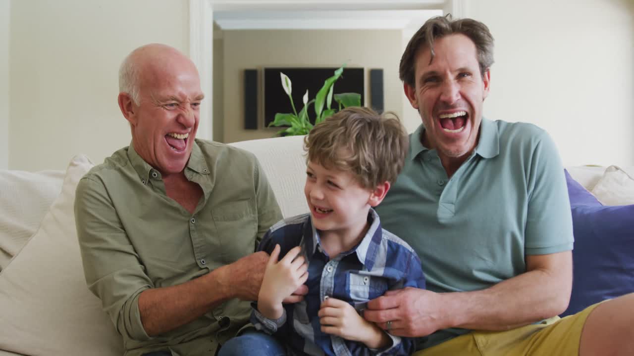 Portrait of happy caucasian grandfather with adult son and grandson playing in living room