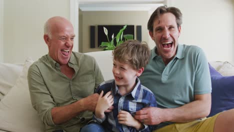 retrato de un abuelo caucásico feliz con un hijo adulto y un nieto jugando en la sala de estar