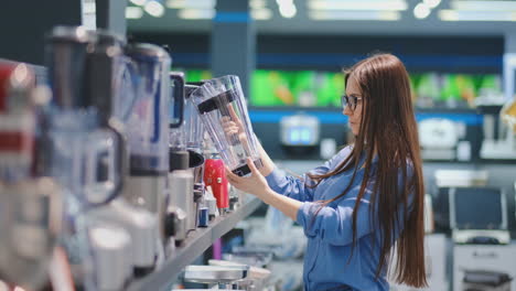 In-the-appliances-store,-a-brunette-woman-in-a-shirt-chooses-a-blender-for-shopping-by-viewing-and-holding-the-device-in-her-hands.