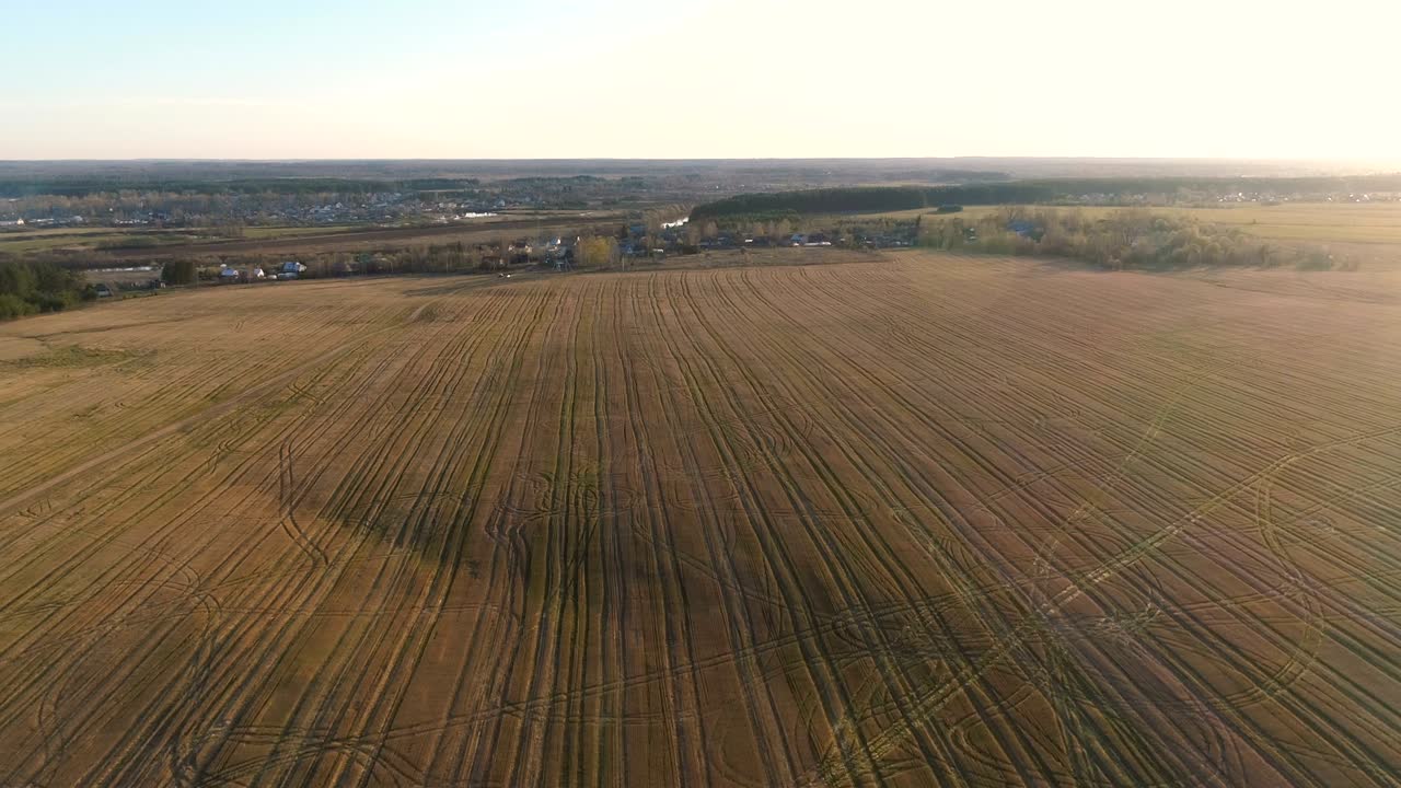 Flight above countryside green fields, forest, and village early spring, aerial panoramic view.