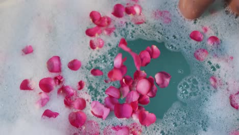 african american woman taking bath and touching flower petals in water in bathroom