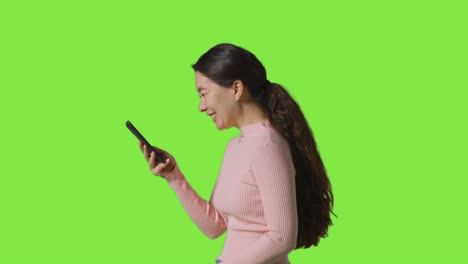 fotografía de perfil de estudio de una mujer sonriente usando un teléfono móvil contra una pantalla verde