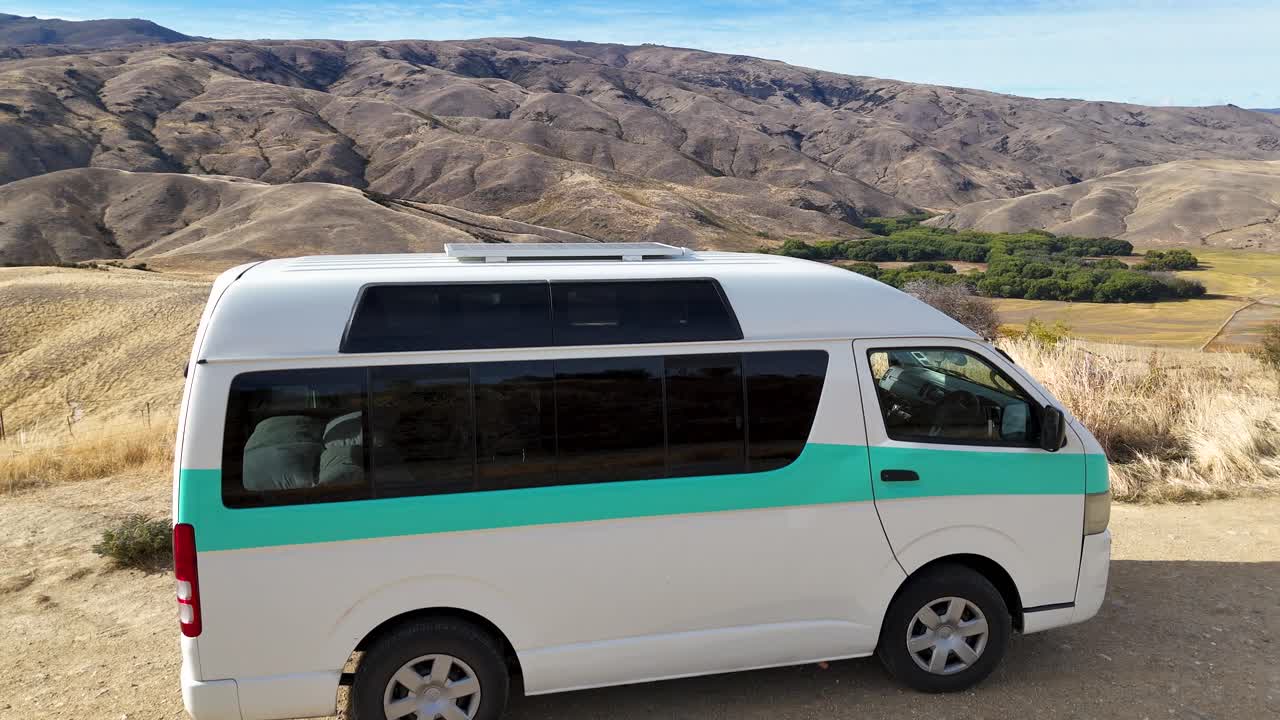 A 4K drone hovers over a camper van at Lindis Pass, New Zealand. Drone captures rolling hills, and dramatic mountains in the South Island