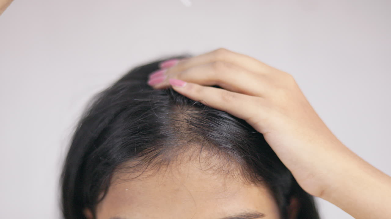 A woman with a dropper applying hair serum on scalp in white background.