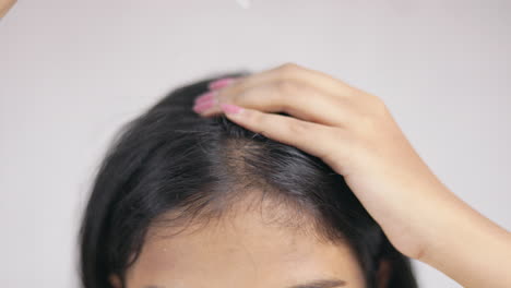 a woman with a dropper applying hair serum on scalp in white background.