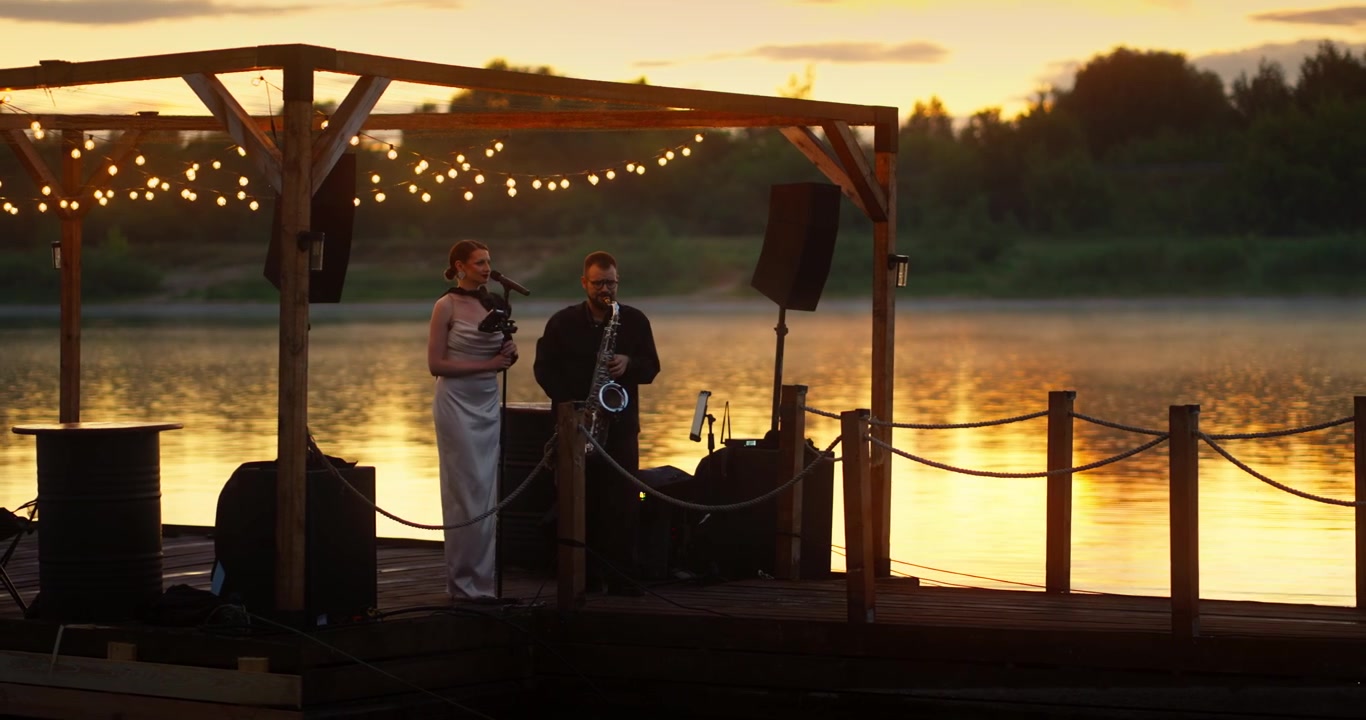 Duo musicale che si esibisce su un molo di legno al tramonto