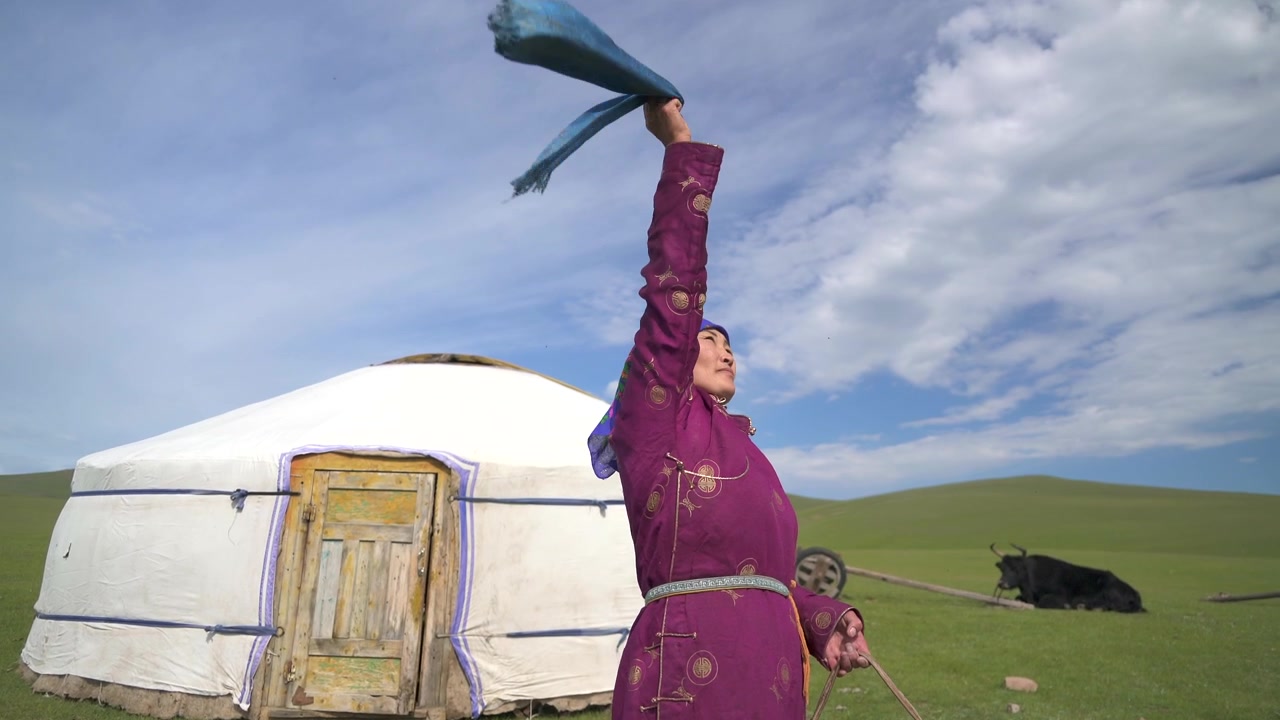 Mongolsk kvinde i traditionel beklædning kærner mælk uden for en ger