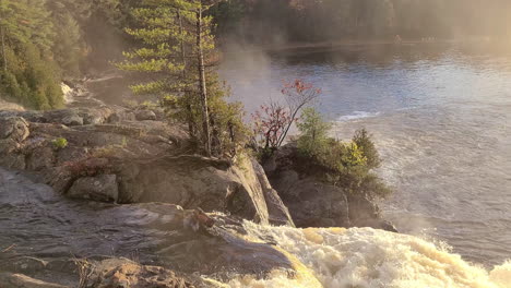 pan of small waterfall, forest and mist over lake in autumn in canada