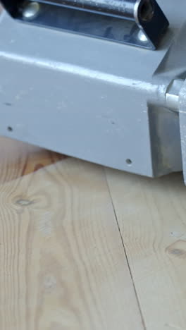 extreme close-up shows a floor sander in reverse motion on pine wood, highlighting clean vs unsanded surface contrast and wood grain clarity, vertical framing, static camera, slow motion