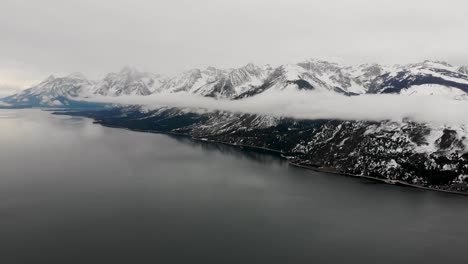 A-high-flying-drone-shot-over-Jackson-Lake-with-the-Teton-Range-in-the-background,-consumed-by-low-lying-clouds,-in-Grand-Teton-National-Park-of-Northwestern-Wyoming