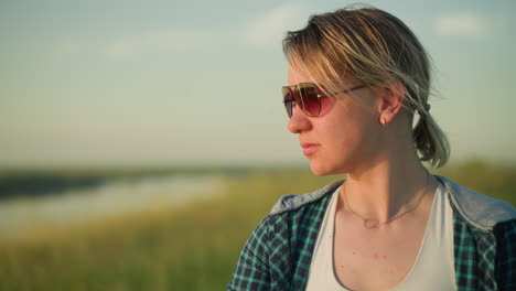 a young woman in a checkered shirt and sunglasses gazes thoughtfully into the distance, with the background beautifully blurred