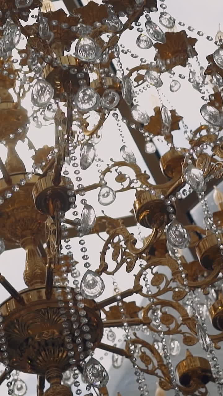 Stylish large vintage luster decorated with crystals and golden carcass hanging on ceiling in room close low angle shot. Antique hall interior design