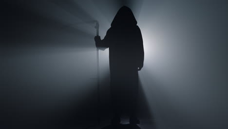 silhouette scary scytheman standing in dark background. grim reaper indoors.