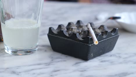 cigarette in ashtray and a glass of drink on a table