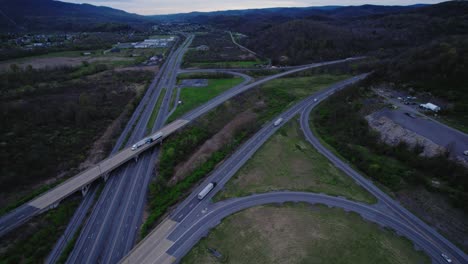 Toma-Aérea-De-Un-Complejo-Cruce-De-Carreteras-Con-Múltiples-Rampas-Y-Carriles-De-Unión-En-Una-Zona-Rural-De-Pensilvania-Durante-El-Crepúsculo