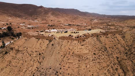 an aerial view of a desert landscape, with a large building situated at the top of a hill or mountain. an old amazigh village,