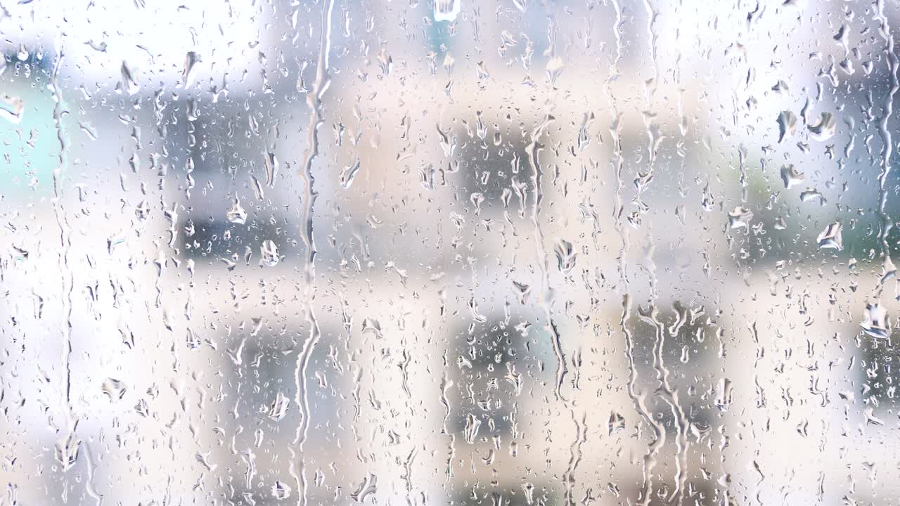Rain drops on window glasses surface with blur building background, 4k movie, slow motion.
