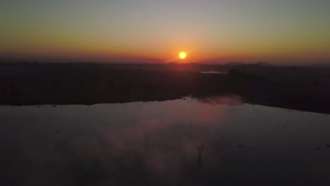 morning sun rises over the african bush creating beautiful colours in the sky and the low lying mist on the lake below.